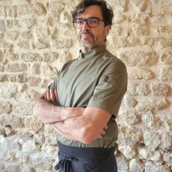 Frédéric Delannoy en tenue de chef devant un mur en pierre